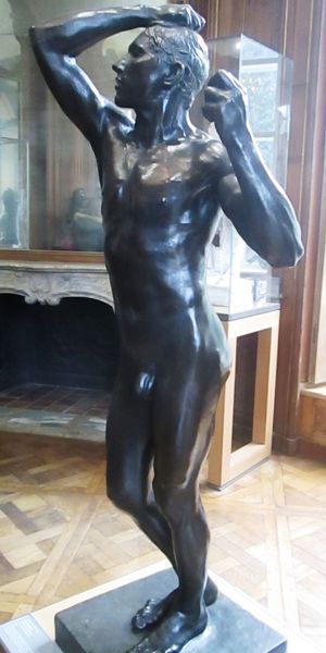 Statue en bronze d'homme nu debout, les bras orientés vers le haut, une main dans les cheveux.