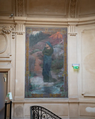 Femme habillée d'un vêtement sombre à capuche, tête basse, paysage rocheux et forestier.