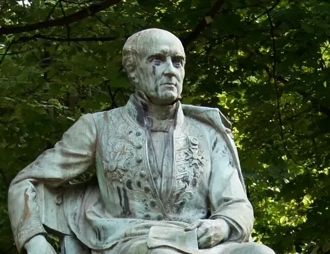 statue d’un homme assis sur une chaise, un bras sur le dossier. Il est habillé d’un vêtement sur lequel sont fixées les décorations qu’il a obtenues.