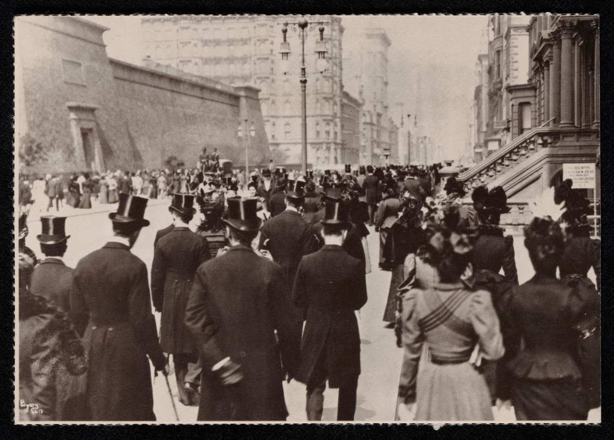 Carte postale montrant une rue urbaine du début du XXe siècle, avec hommes en hauts-de-forme et femmes en robes longues vus de dos.