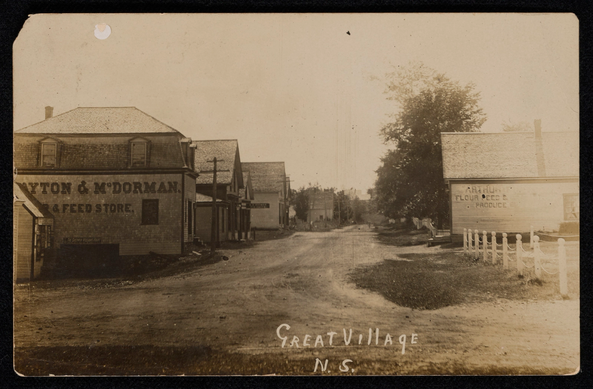 Carte postale ancienne montrant une rue de village bordée de bâtiments en bois, avec l'inscription manuscrite 'Great Village' au bas de l'image.