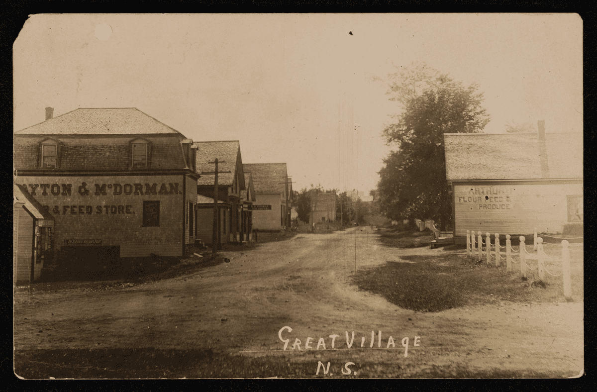 Carte postale ancienne montrant une rue de village bordée de bâtiments en bois, avec l'inscription manuscrite 'Great Village' au bas de l'image.