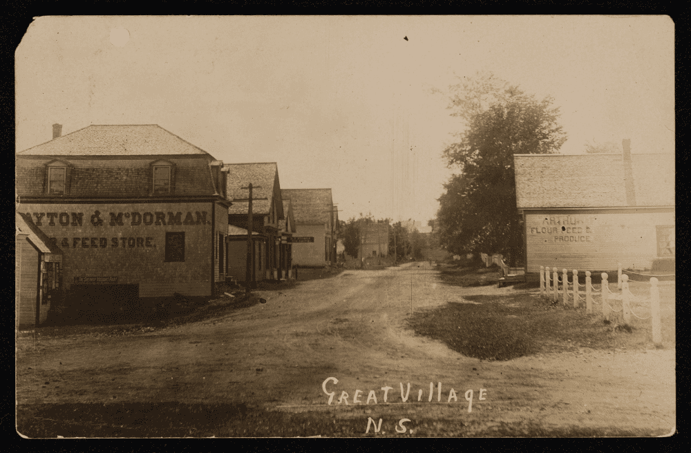 Carte postale ancienne montrant une rue de village bordée de bâtiments en bois, avec l'inscription manuscrite 'Great Village' au bas de l'image.