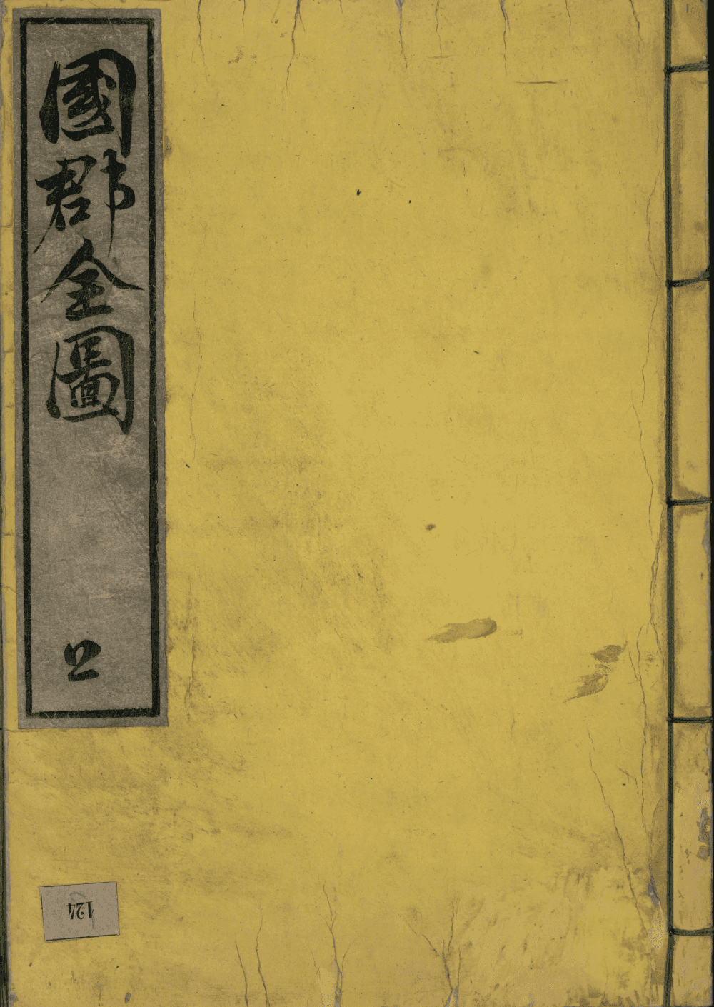 Plat supérieur d'un volume relié à la japonaise : papier washi jaune vieilli, pièce de titre calligraphiée à l'encre noire sur fond gris en bandeau vertical gauche, couture à cinq piqûres apparente sur le côté droit.