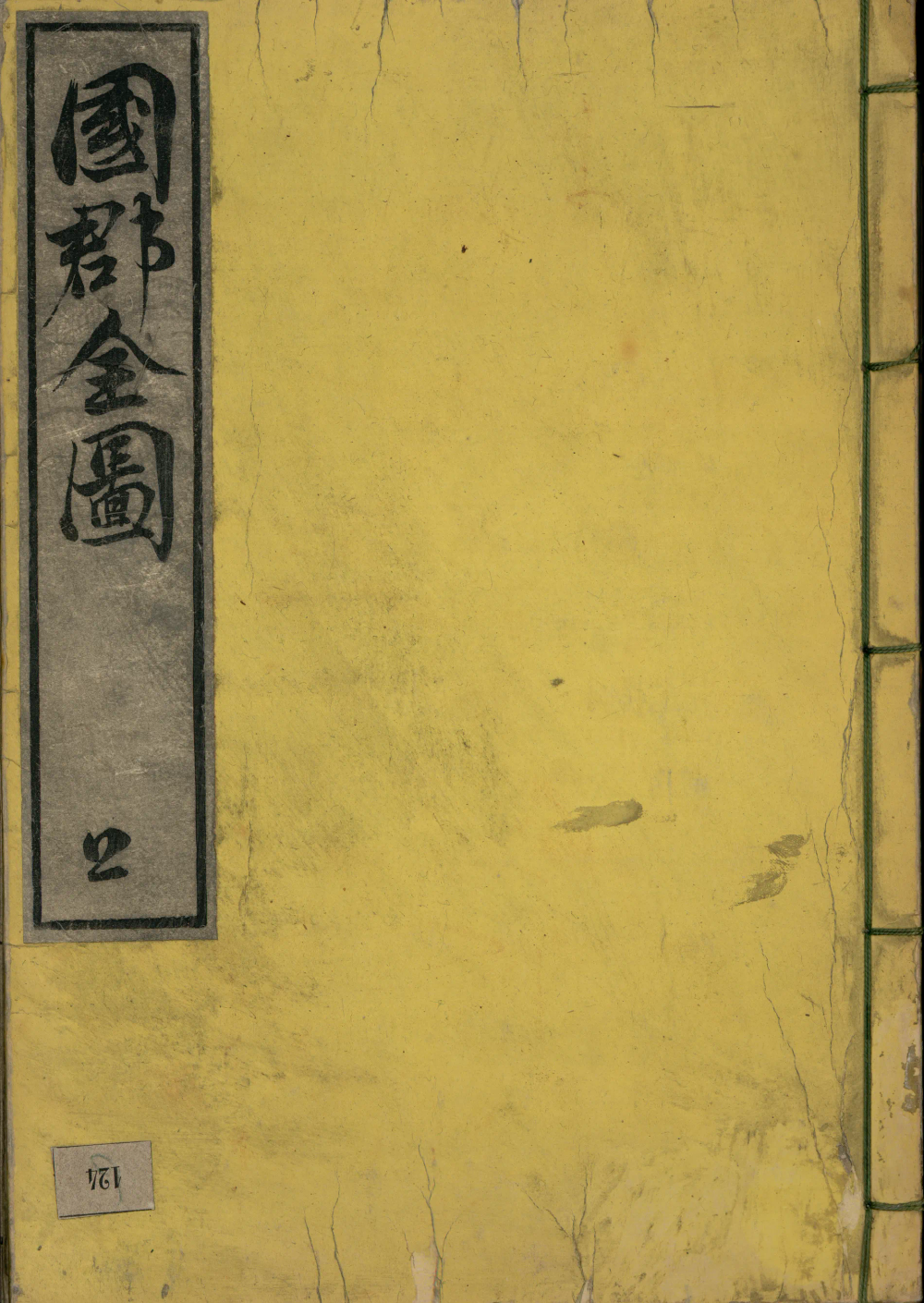 Plat supérieur d'un volume relié à la japonaise : papier washi jaune vieilli, pièce de titre calligraphiée à l'encre noire sur fond gris en bandeau vertical gauche, couture à cinq piqûres apparente sur le côté droit.