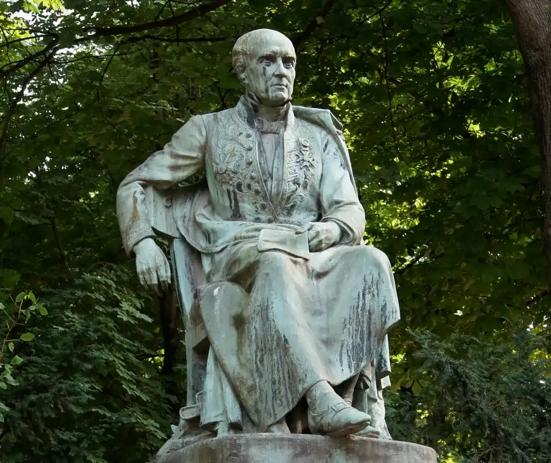 statue d’un homme assis sur une chaise, un bras sur le dossier. Il est habillé d’un vêtement sur lequel sont fixées les décorations qu’il a obtenues.