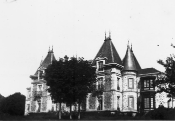 Photographie en noir et blanc d'un château vu de trois quarts, arbres devant la façade.
